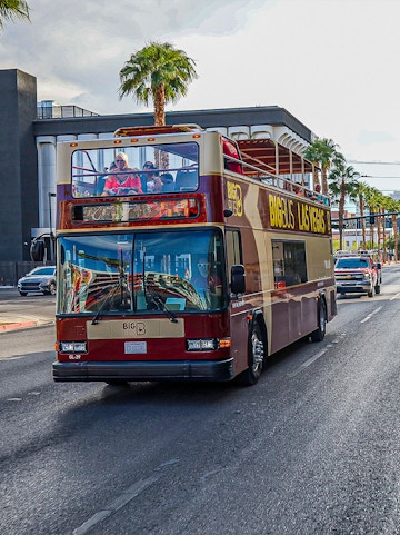 Open-top Big Bus tour driving on Las Vegas Boulevard with palm trees in the background.