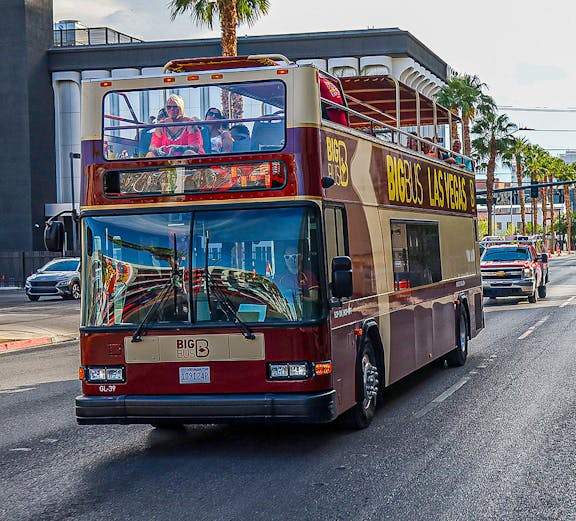 Open-top Big Bus tour driving on Las Vegas Boulevard with palm trees in the background.