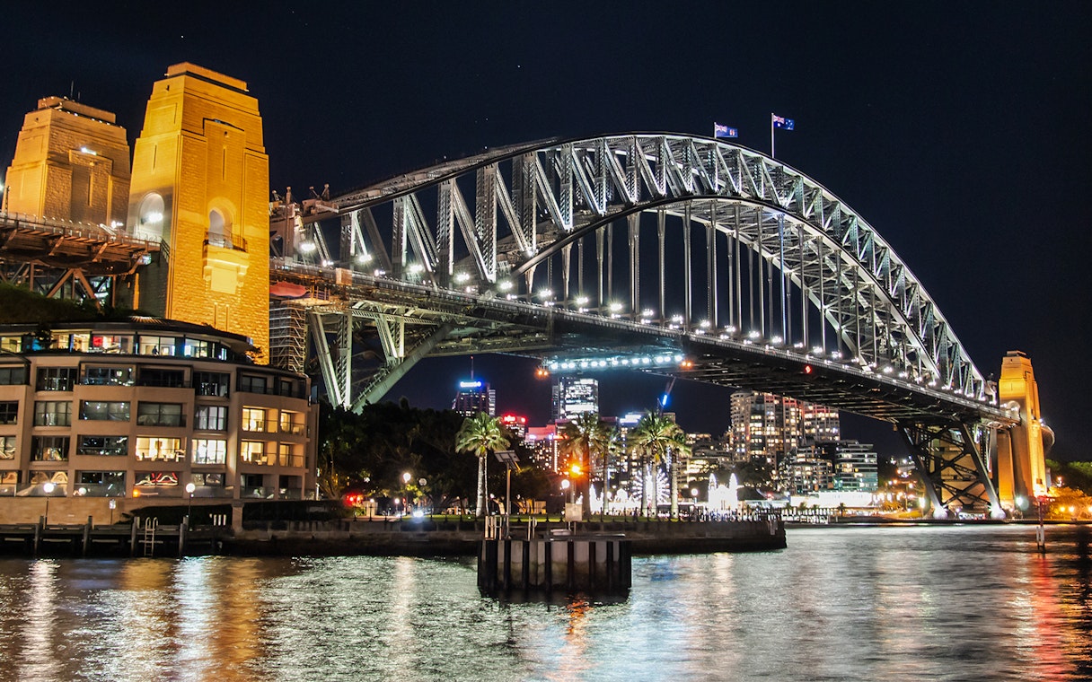 Sydney Harbour Bridge illuminated at night with city skyline in the background.