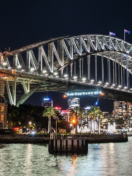 Sydney Harbour Bridge illuminated at night with city skyline in the background.