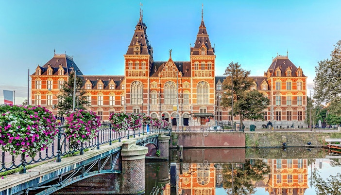 Rijksmuseum exterior with canal and flower-lined bridge, Amsterdam.