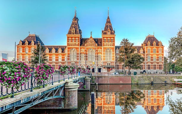 Rijksmuseum exterior with canal and flower-lined bridge, Amsterdam.