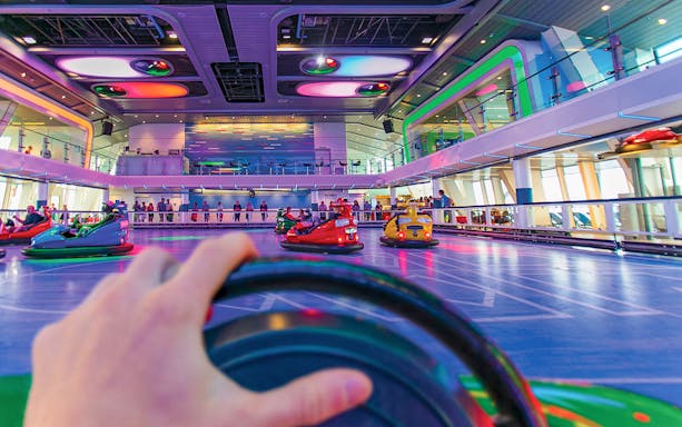 Bumper cars on a cruise ship deck with colorful lights and passengers watching.