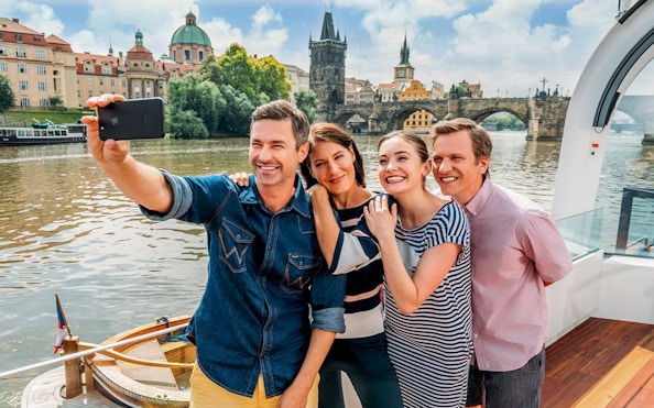 Group taking selfie on Vltava River cruise with Charles Bridge in Prague.