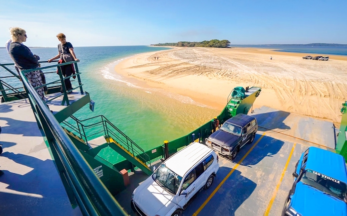 Ferry with vehicles approaching Fraser Island's sandy shore, K'gari.