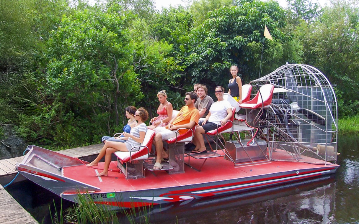 Tourists seated on an airboat in Everglades National Park, surrounded by lush greenery.