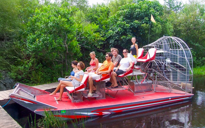 Tourists seated on an airboat in Everglades National Park, surrounded by lush greenery.