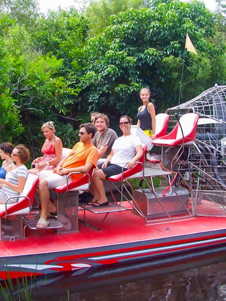Tourists seated on an airboat in Everglades National Park, surrounded by lush greenery.