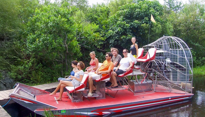 Tourists seated on an airboat in Everglades National Park, surrounded by lush greenery.