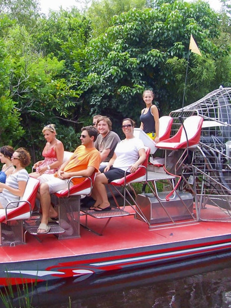 Tourists seated on an airboat in Everglades National Park, surrounded by lush greenery.