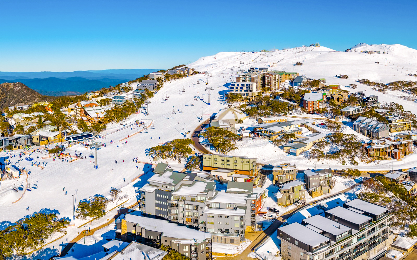Skiers on slopes at Mt Buller, Australia, with snow-covered buildings and mountains in the background.
