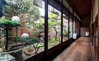 Kyoto machiya interior with traditional garden view, featuring bonsai trees and wooden walkway.
