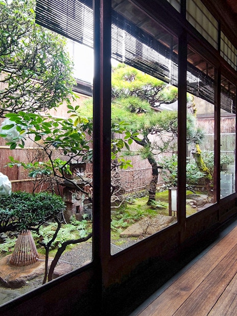 Kyoto machiya interior with traditional garden view, featuring bonsai trees and wooden walkway.