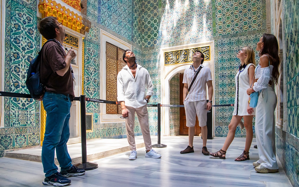 Tourists admiring ornate tilework inside Topkapi Palace, Istanbul.