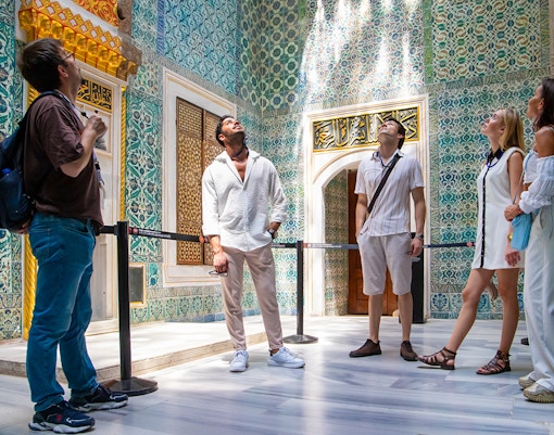 Tourists admiring ornate tilework inside Topkapi Palace, Istanbul.