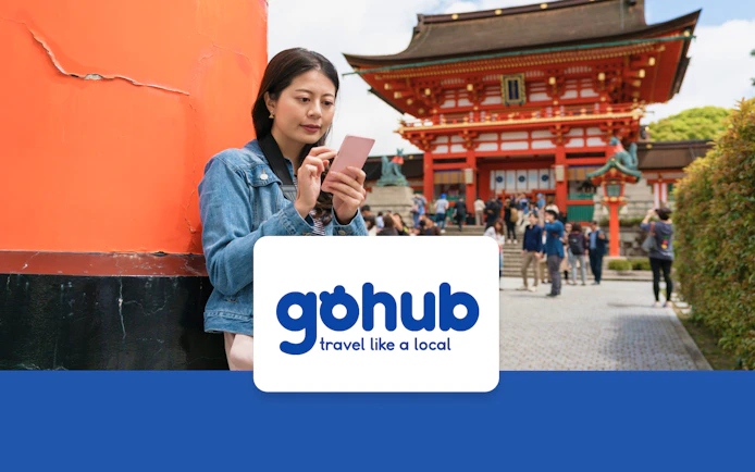 Asian traveler reading guide on phone near Fushimi Inari Taisha Shrine, Kyoto.