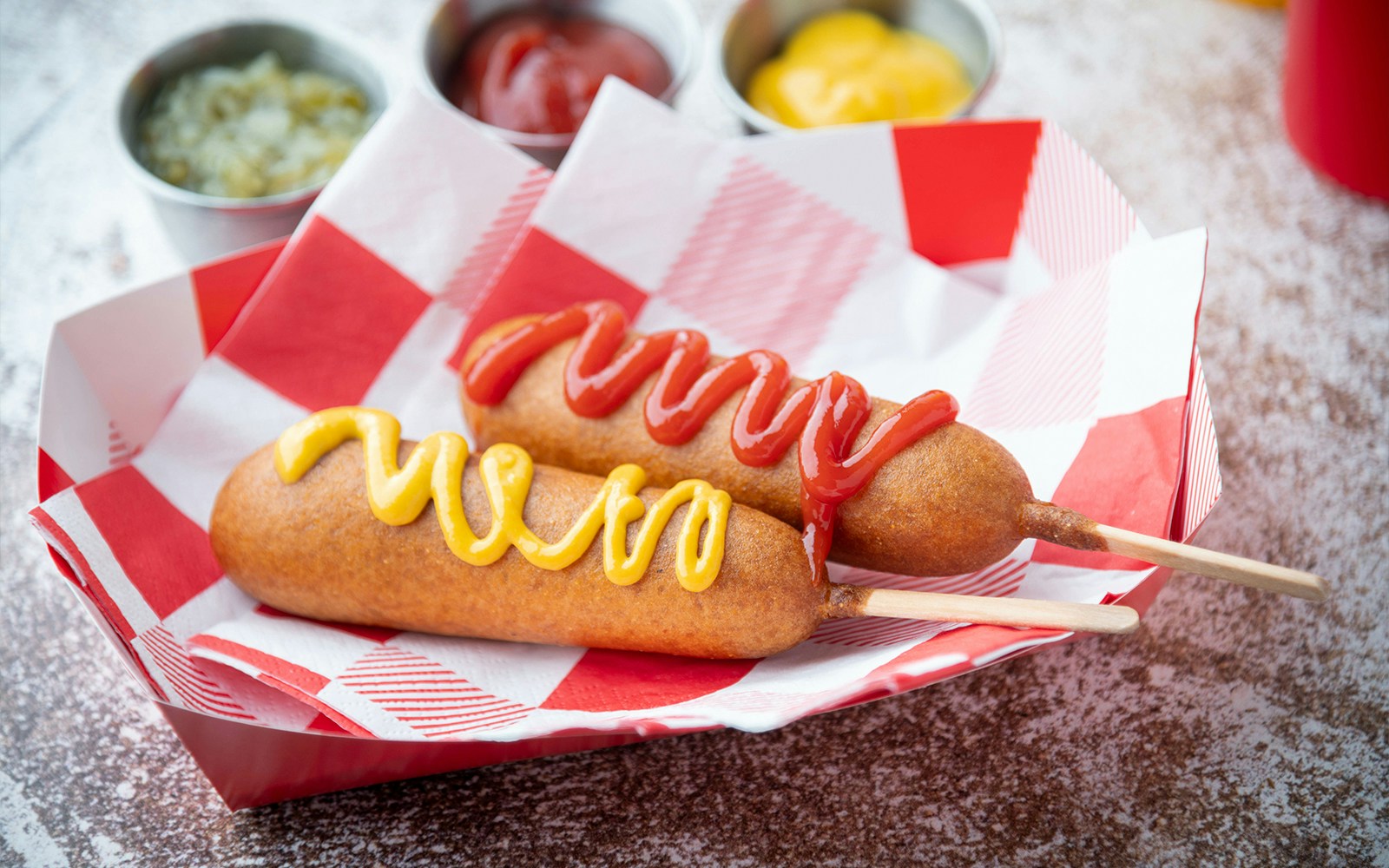 Corn dog topped with ketchup and yellow mustard on a stick.
