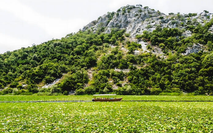 Wooden boat on Lake Skadar with lush green hills in the background.