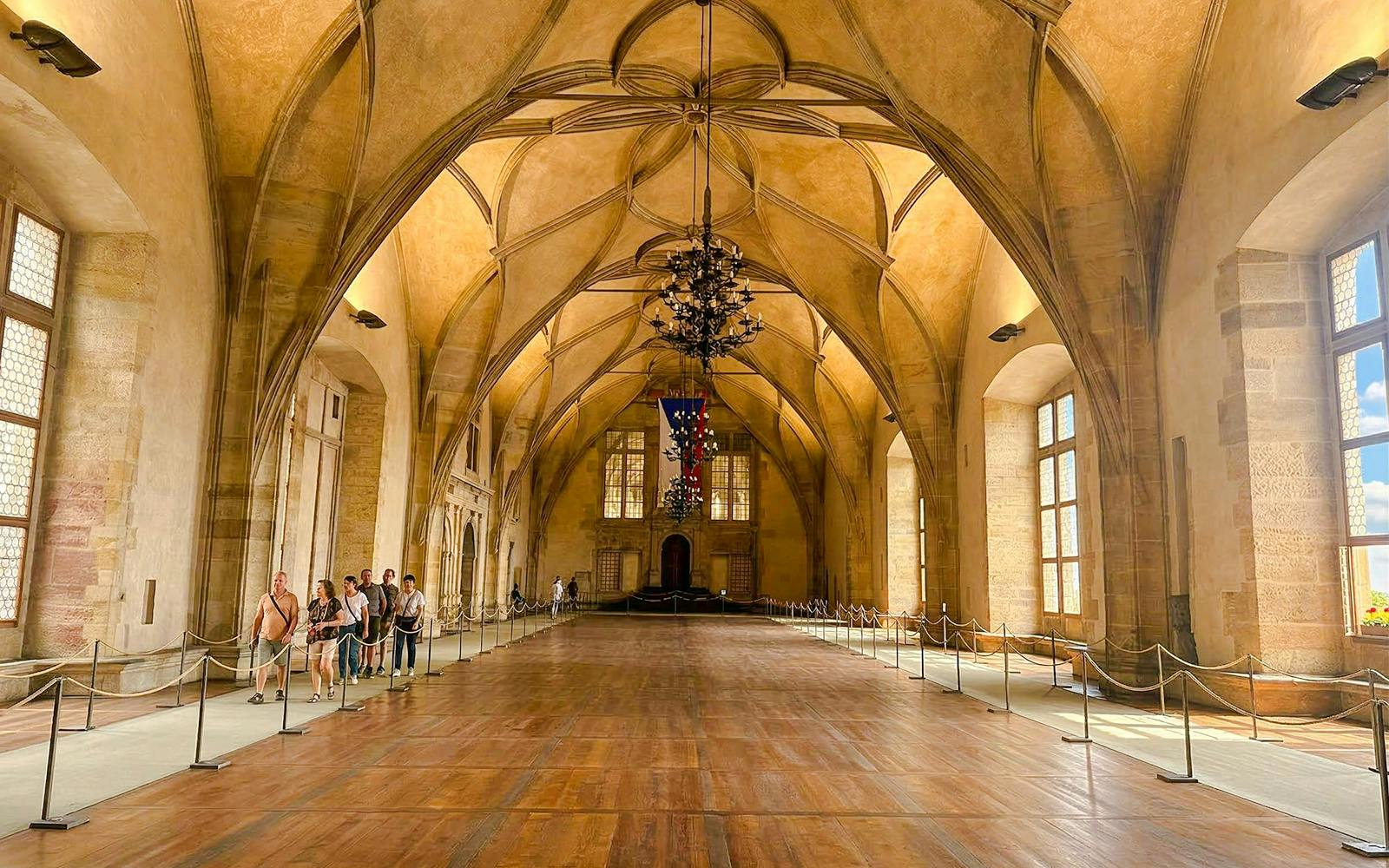 Visitors touring the grand hall of Prague Castle with vaulted ceilings.