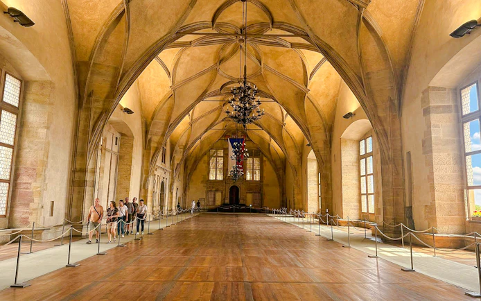 Visitors touring the grand hall of Prague Castle with vaulted ceilings.