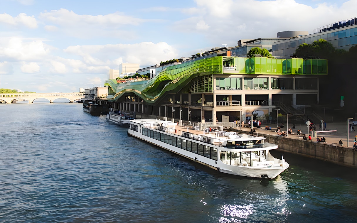 Seine River cruise boat docked near modern green building in Paris.