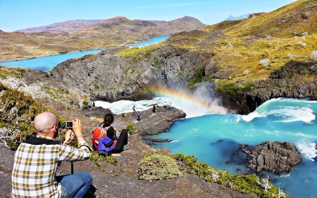 Tourists photographing a waterfall and rainbow in Torres del Paine National Park, Chile.