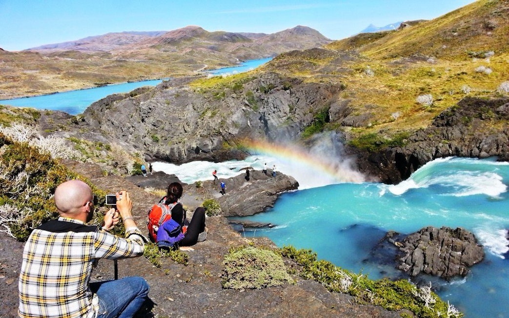 Tourists photographing a waterfall and rainbow in Torres del Paine National Park, Chile.