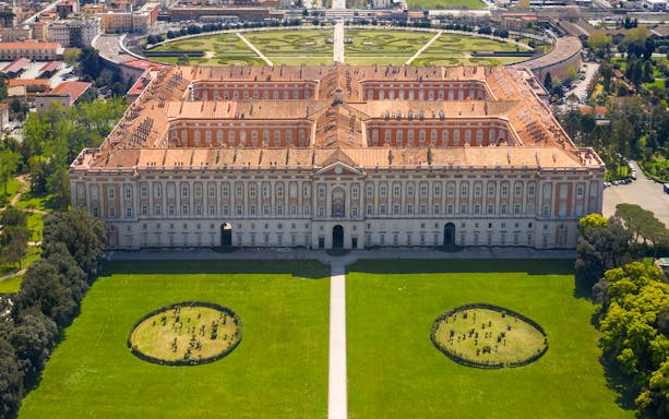 Royal Palace of Caserta aerial view with gardens and surrounding cityscape.