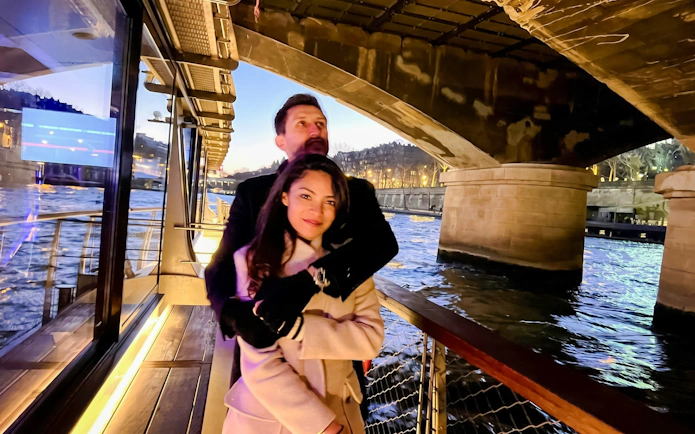 Couple enjoying a Seine River cruise under a bridge in Paris at dusk.