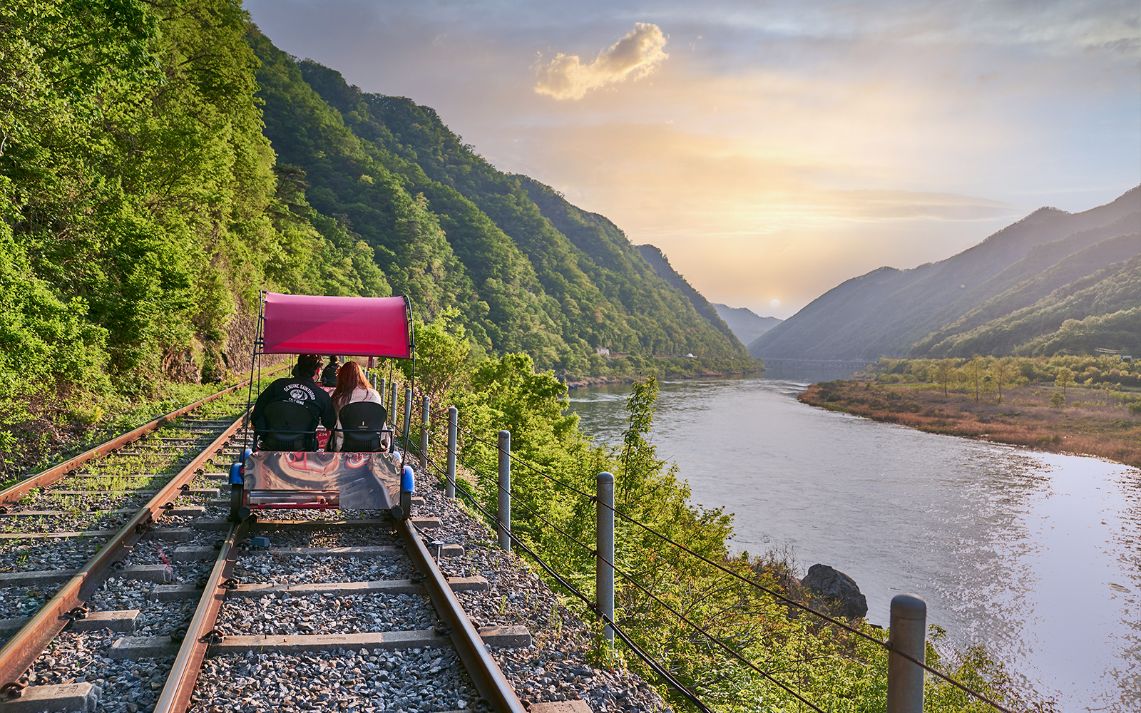 Couple riding Gangchon Railbike along scenic river and mountains at sunset in Korea.