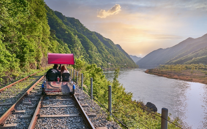 Couple riding Gangchon Railbike along scenic river and mountains at sunset in Korea.