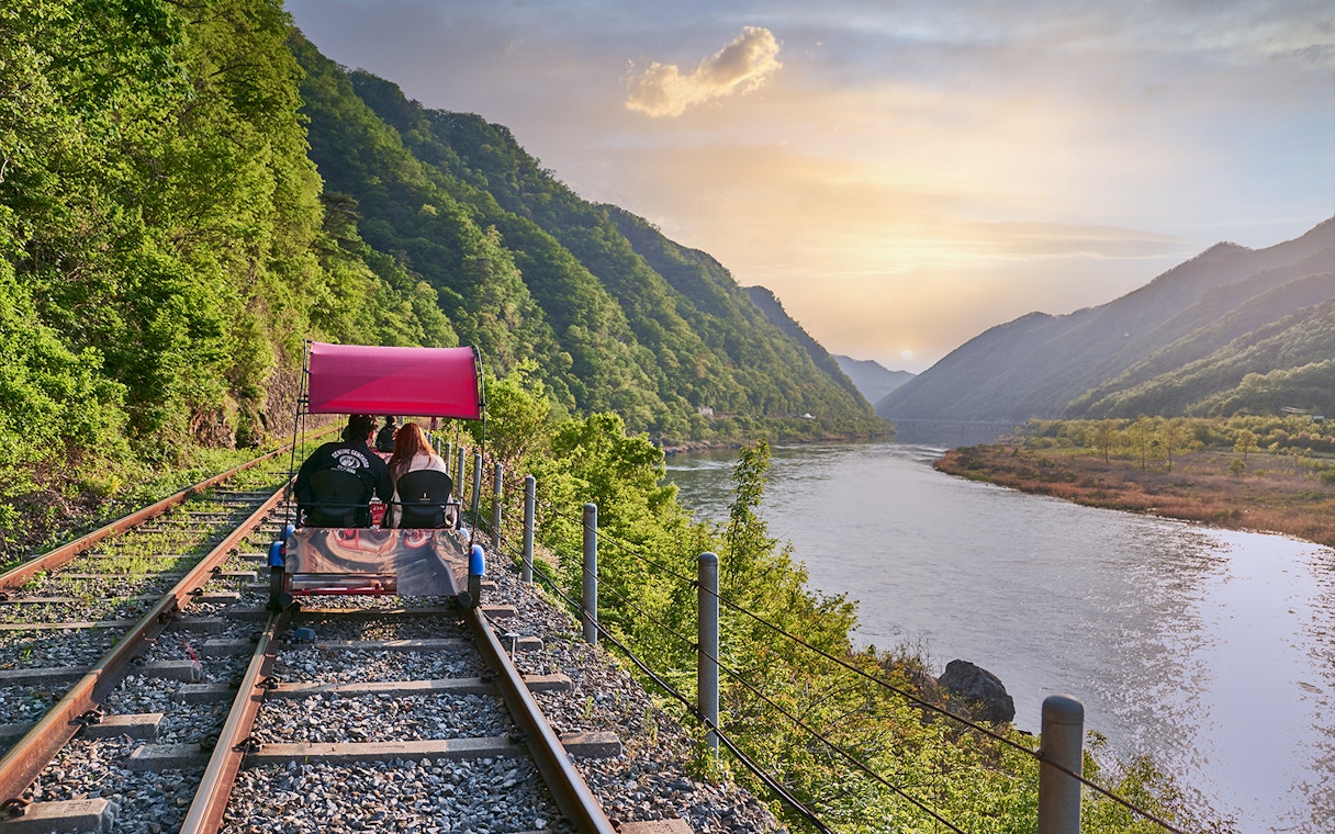 Couple riding Gangchon Railbike along scenic river and mountains at sunset in Korea.