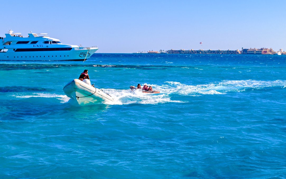 Tubing behind speedboat on Red Sea, Hurghada with yacht in background.