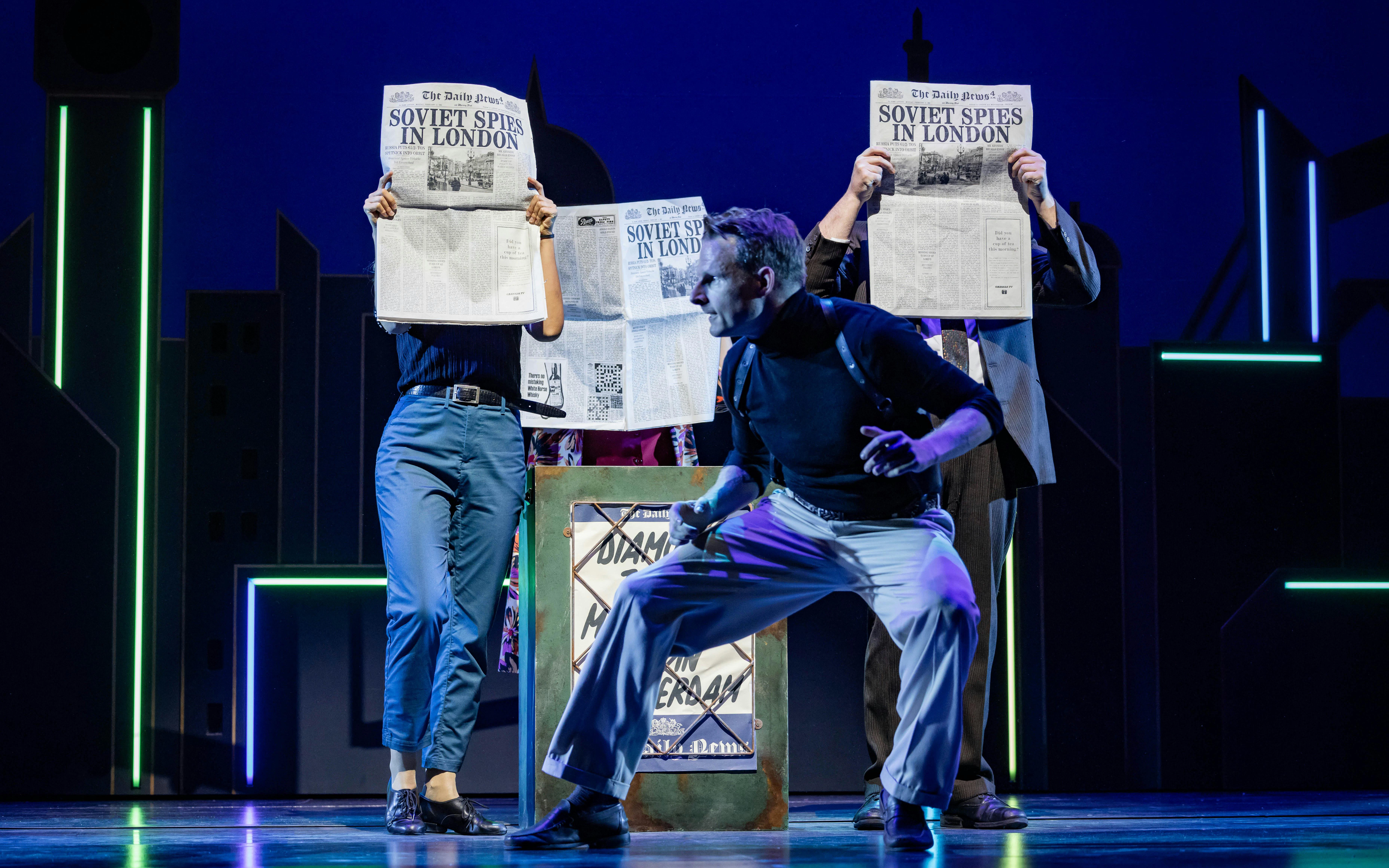Actors on stage holding newspapers with "Soviet Spies in London" headline during The Comedy About Spies performance.