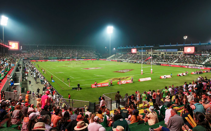 Crowd watching a rugby match at Emirates Dubai 7s stadium at night.