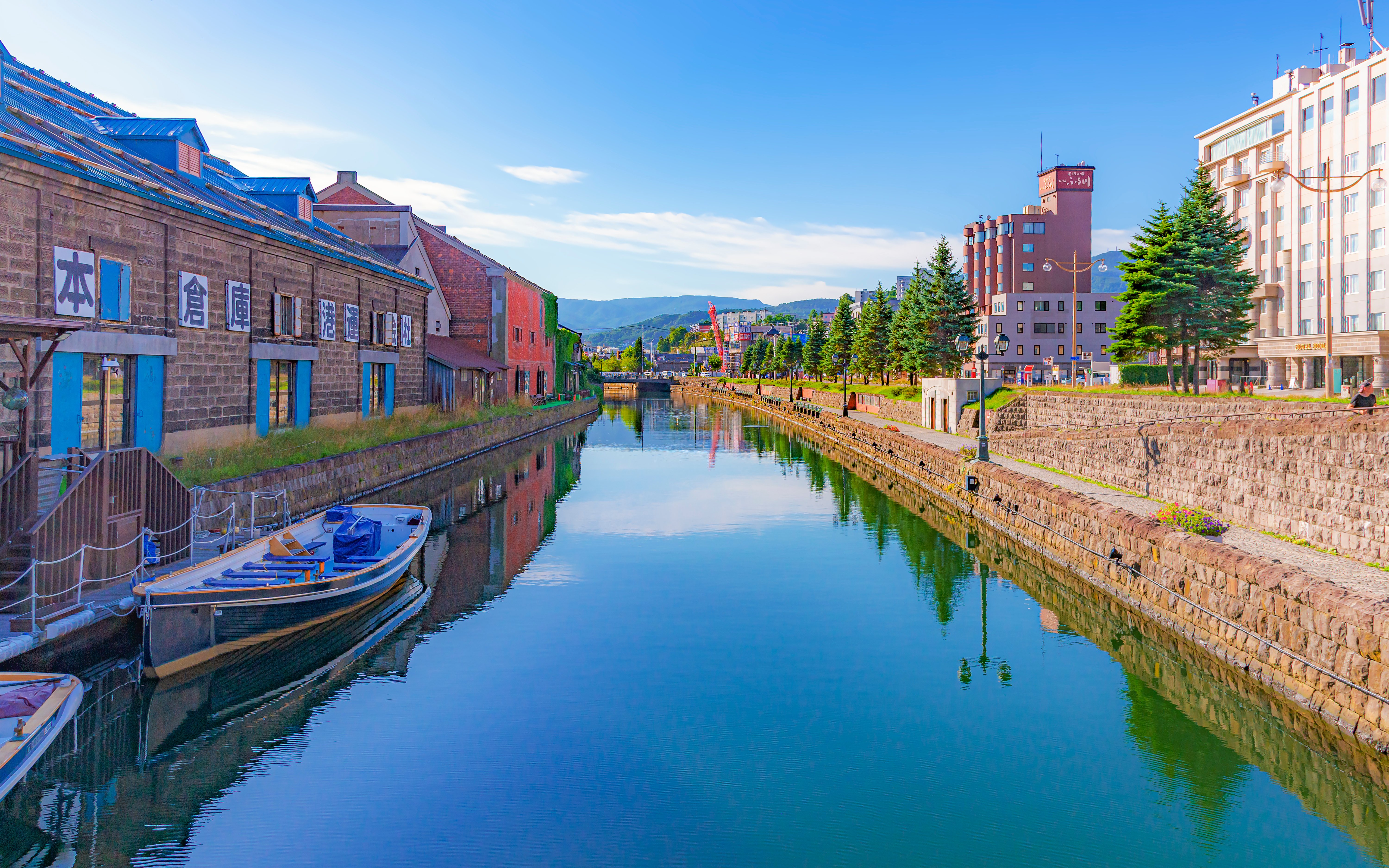 Otaru Canal with historic warehouses and boats under a clear blue sky in summer.