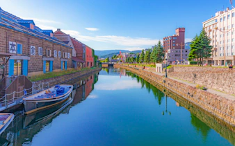 Otaru Canal with historic warehouses and boats under a clear blue sky in summer.