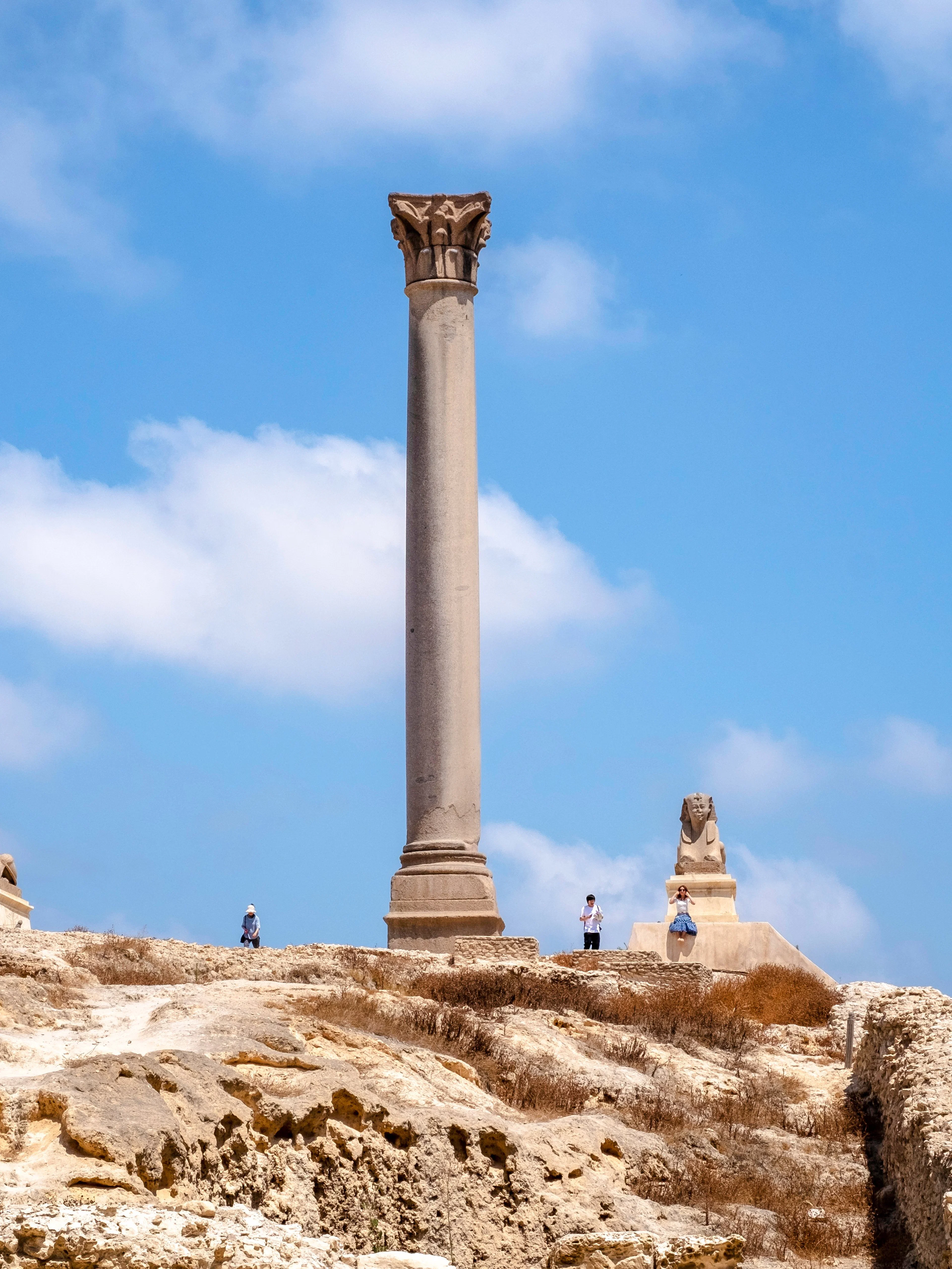Pompey's Pillar in Alexandria, Egypt, with surrounding ruins and sphinx statues.