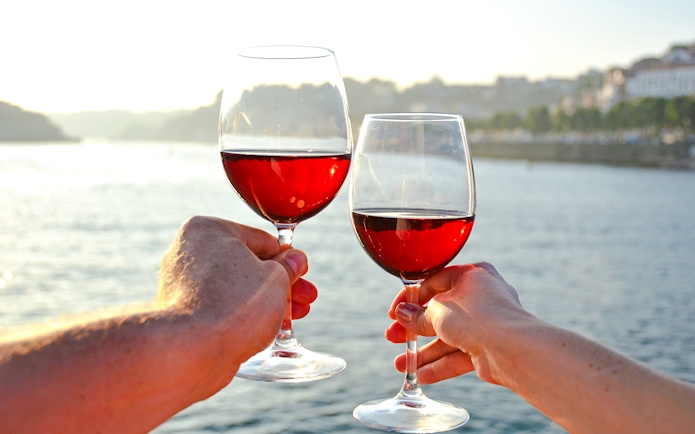 Tourists holding wine glasses by a riverside.