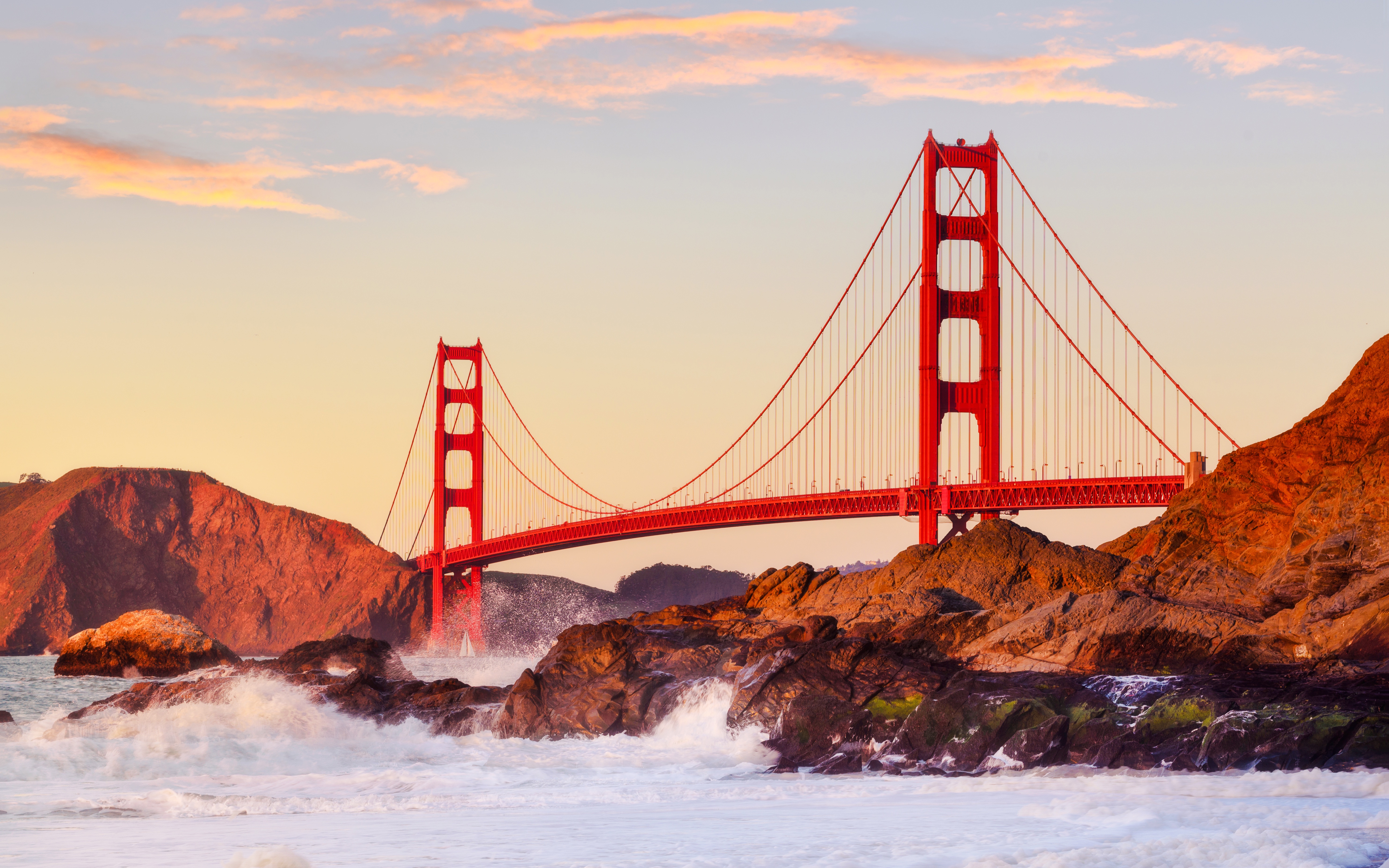 Golden Gate Bridge at sunset with waves crashing on rocks, San Francisco.