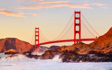 Golden Gate Bridge at sunset with waves crashing on rocks, San Francisco.
