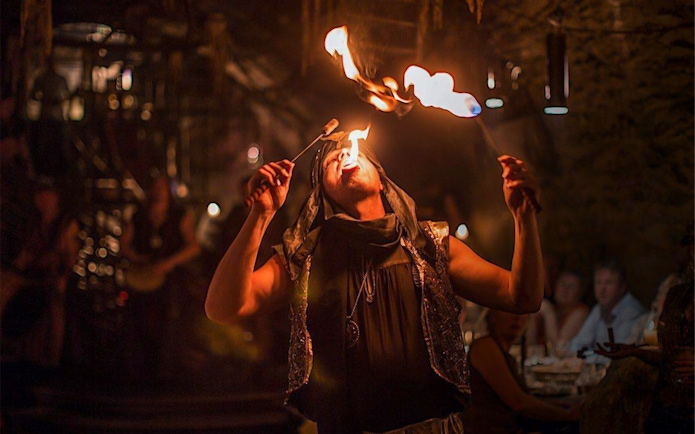Fire performer at a medieval dinner show entertaining guests with fire-eating act.