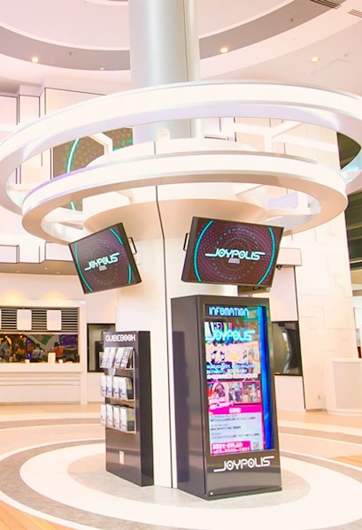 Joypolis information kiosk with digital screens in a modern indoor setting.