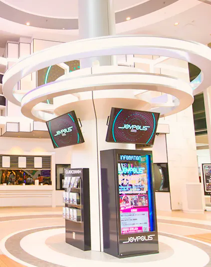 Joypolis information kiosk with digital screens in a modern indoor setting.