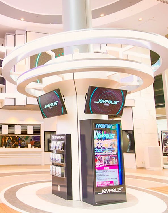 Joypolis information kiosk with digital screens in a modern indoor setting.