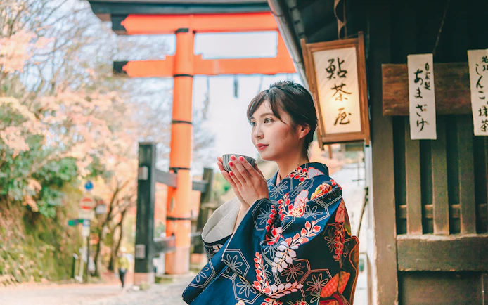 Person in kimono holding a cup near Fushimi Inari Shrine, Kyoto.