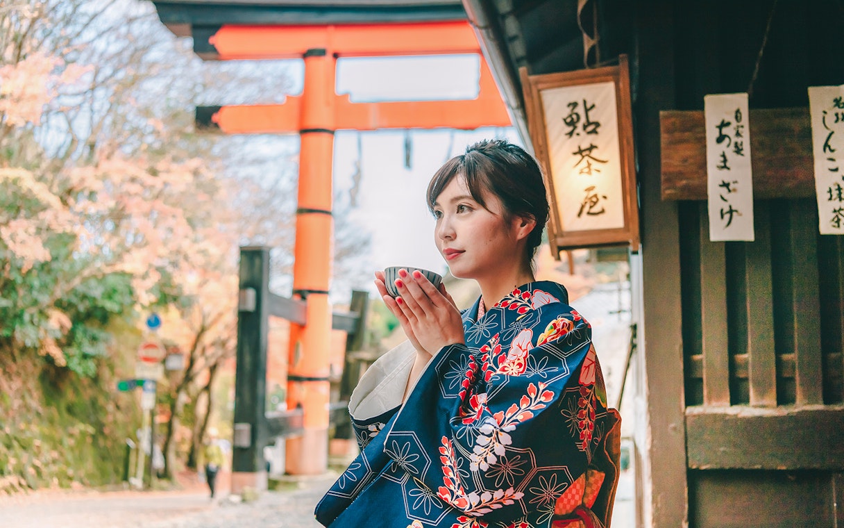 Person in kimono holding a cup near Fushimi Inari Shrine, Kyoto.