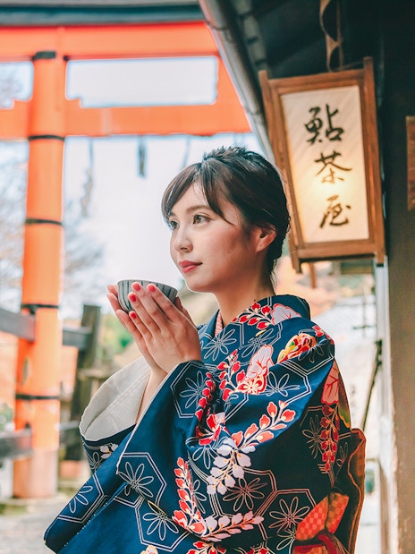 Person in kimono holding a cup near Fushimi Inari Shrine, Kyoto.