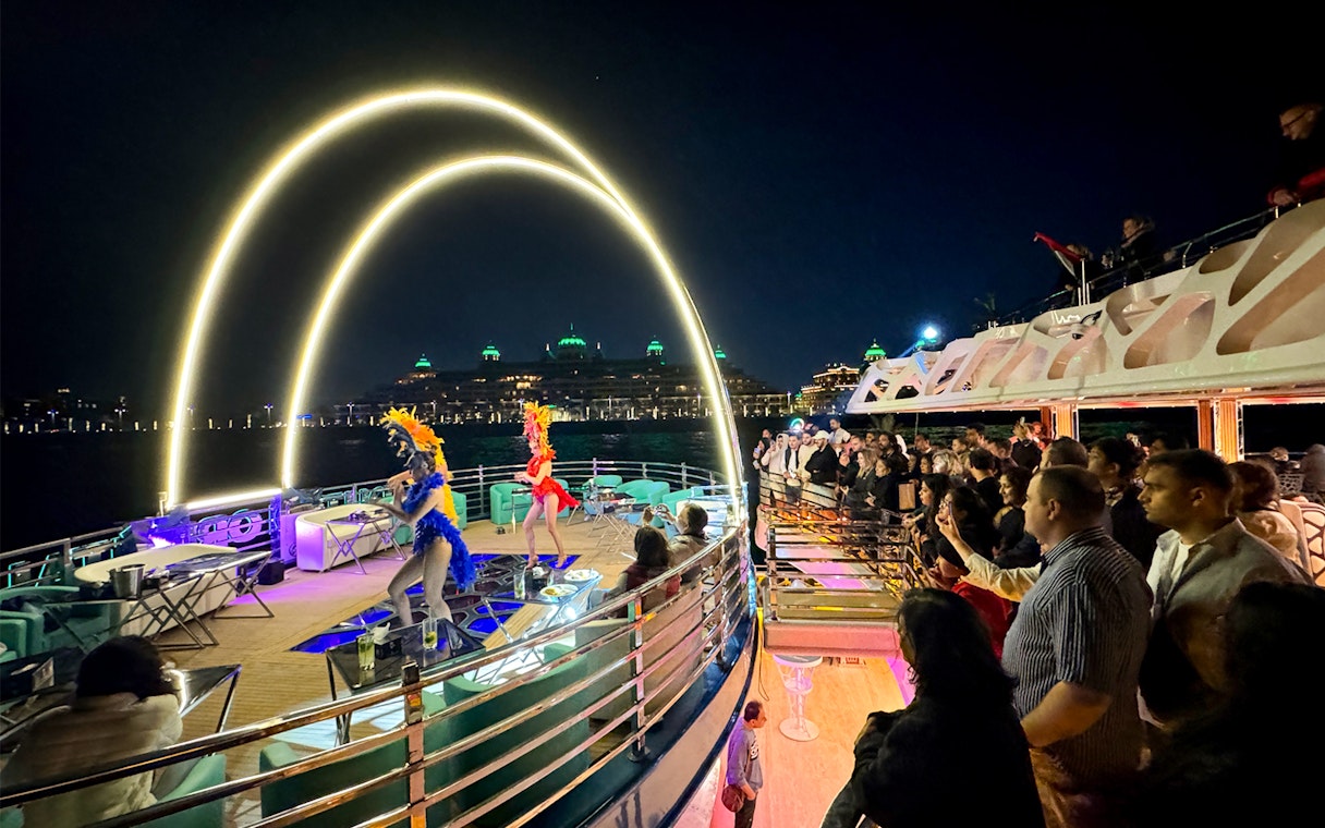 Performers entertaining guests on a cruise ship at night with city lights in the background.