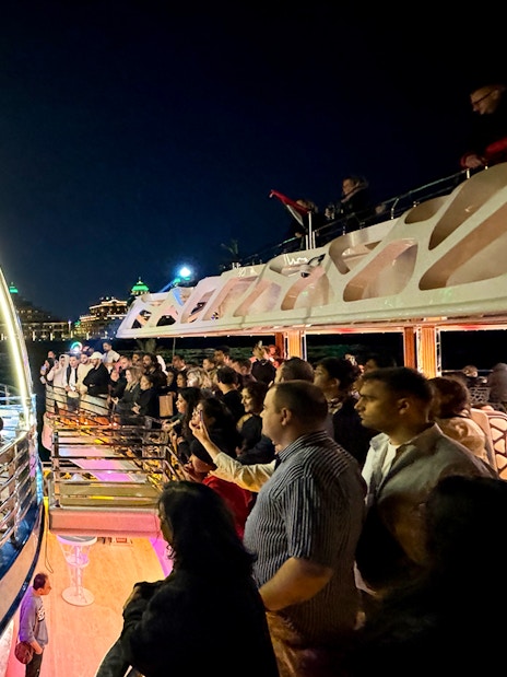 Performers entertaining guests on a cruise ship at night with city lights in the background.